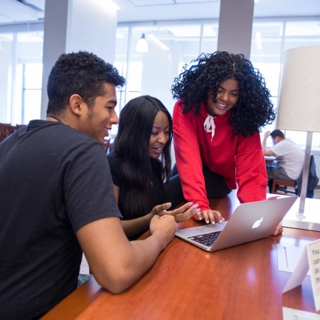 Three students looking at a laptop together